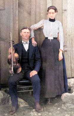 Charlie Lohman seated with fiddle, Ellen Dora standing beside him