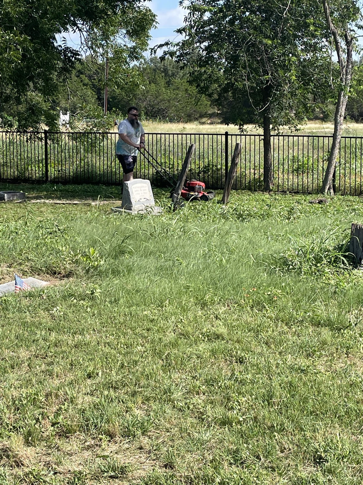 A volunteer mows between rows of headstones in the late-day sun.